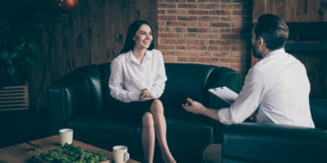 Photo of two business people lady man share news drink hot coffee mug, beverage chatting friendly interview ask answer questions formalwear clothes sit couch modern office indoors